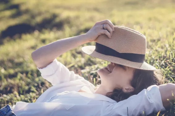 A woman in hat lying on green grass with closed eyes enjoying summer sun 