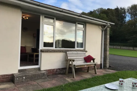 An external view of Fuchsia Cottage at Sprecombe Holiday Cottages with a bench and picnic table