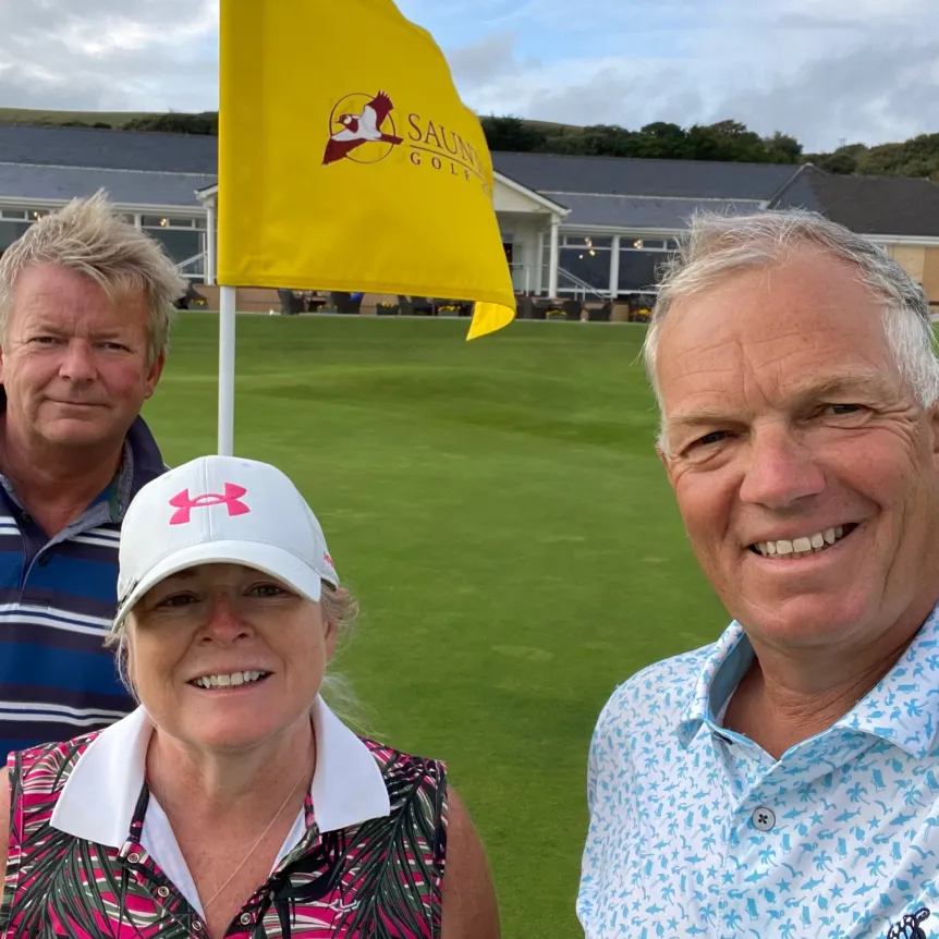 Three golfers outside Saunton Sands clubhouse by the final hole