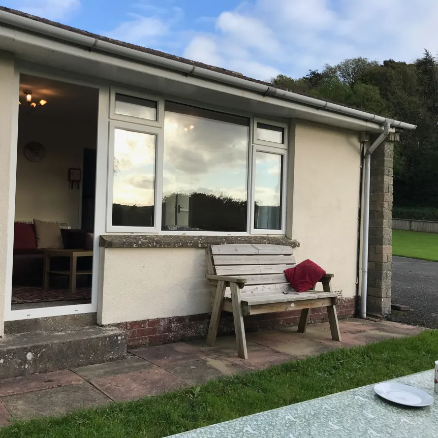 An external view of Fuchsia Cottage at Sprecombe Holiday Cottages with a bench and picnic table