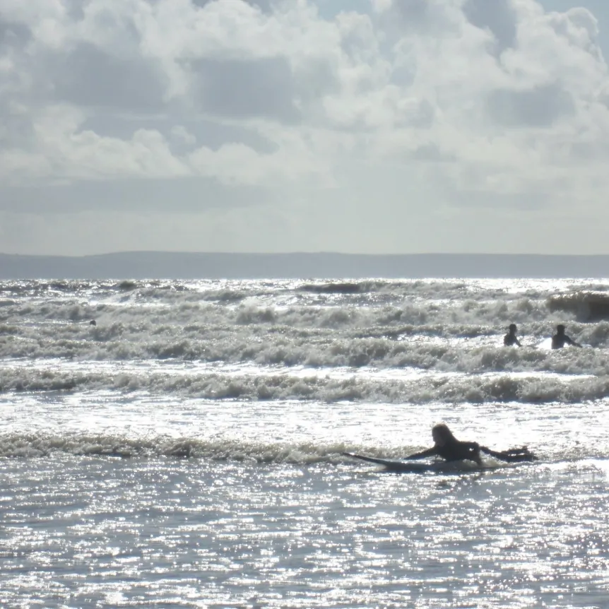 Several people surfing in a brightly lit sea with lots of waves