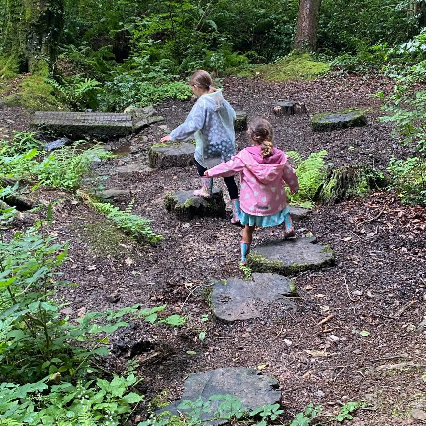 Children wearing coats playing on stepping stones in a woodland clearing
