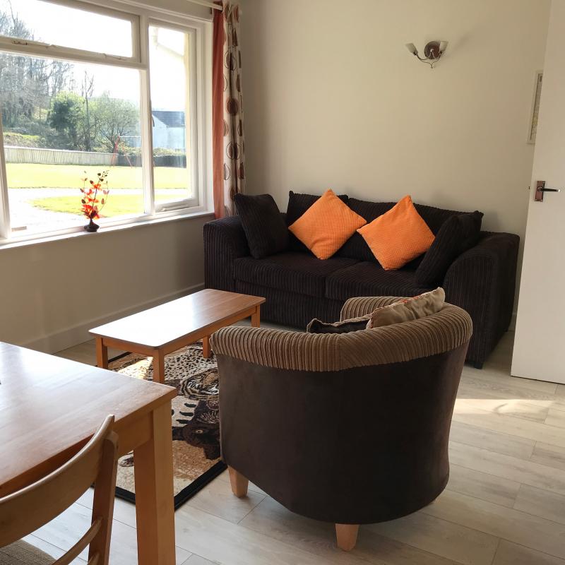 Newly floored Begonia Begonia Lounge showing 3 seater sofa, wood laminate floor and tub chair